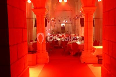 Salle avec des rangées de chaises rouges alignées sur un tapis rouge, entourée de colonnes et éclairée par des projecteurs.