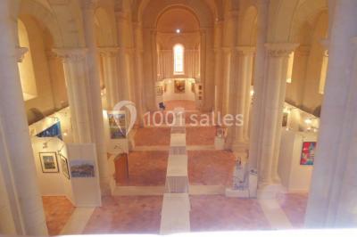 Salle avec des rangées de chaises rouges alignées sur un tapis rouge, entourée de colonnes et éclairée par des projecteurs.