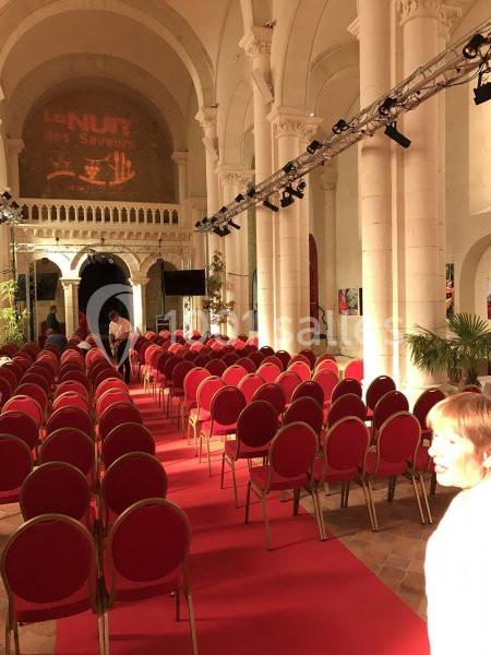Salle voûtée avec des rangées de chaises rouges alignées sur un tapis rouge, éclairée pour un événement.