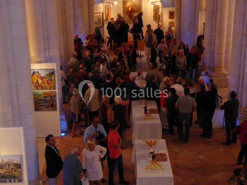 Groupe de personnes rassemblées dans une salle voûtée, entourées de peintures exposées et de tables de réception.