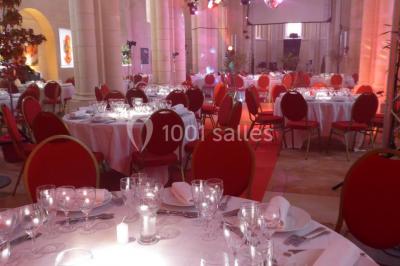 Salle avec des rangées de chaises rouges alignées sur un tapis rouge, entourée de colonnes et éclairée par des projecteurs.