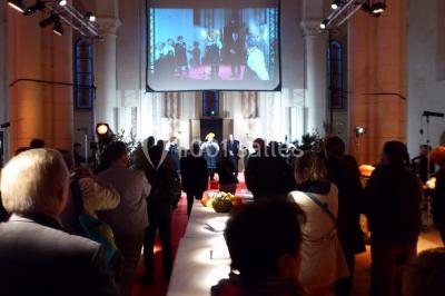 Salle avec des rangées de chaises rouges alignées sur un tapis rouge, entourée de colonnes et éclairée par des projecteurs.
