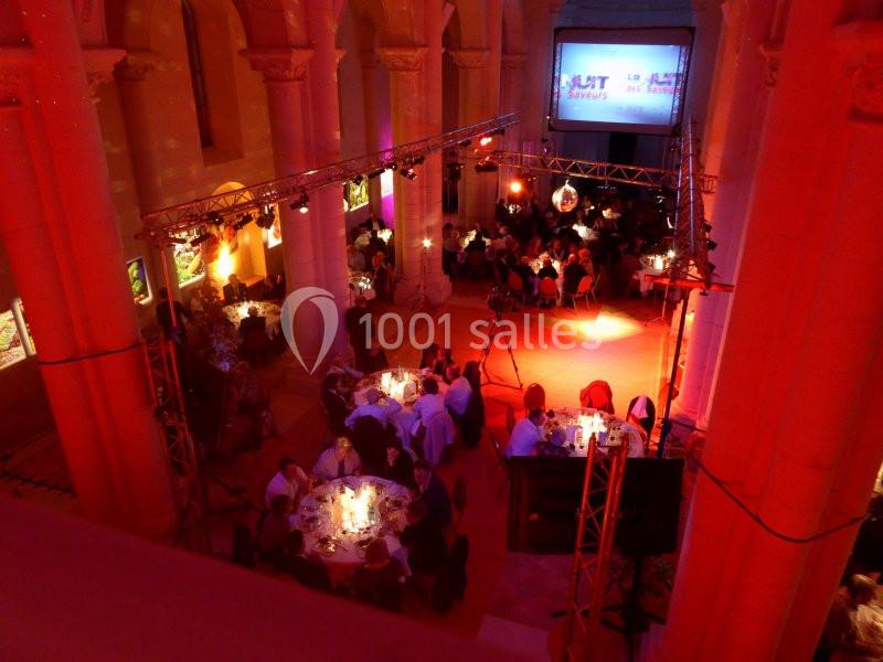 Salle voûtée éclairée en rouge avec des tables rondes dressées pour un dîner, ambiance festive et chaleureuse.