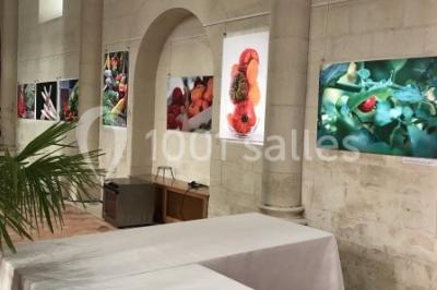 Salle avec des rangées de chaises rouges alignées sur un tapis rouge, entourée de colonnes et éclairée par des projecteurs.