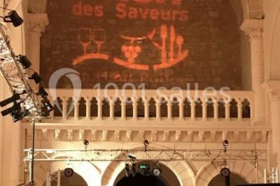 Salle avec des rangées de chaises rouges alignées sur un tapis rouge, entourée de colonnes et éclairée par des projecteurs.