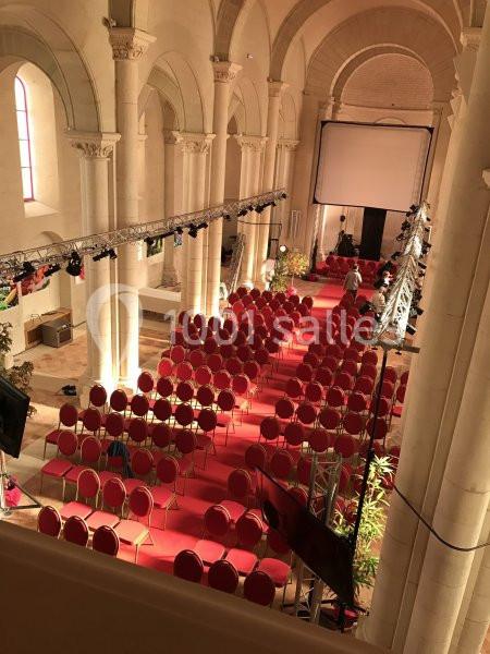 Salle voûtée aménagée avec des rangées de chaises rouges et un écran géant pour un événement ou une projection.