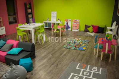 Salle de jeux lumineuse avec une cabane en tissu, un tapis de chiffres, une cuisine pour enfants et des tables colorées.