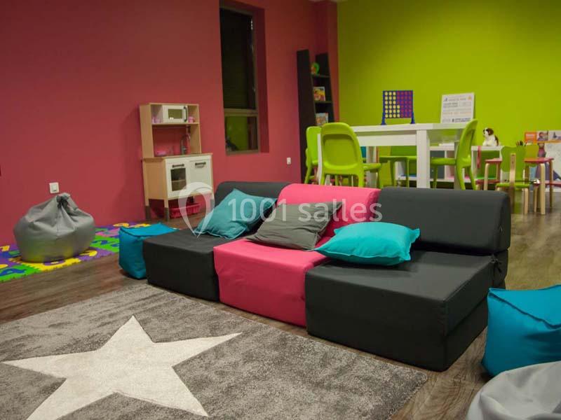 Espace de jeux intérieur coloré avec canapé modulable, tapis étoilé, table, chaises et jouets pour enfants.