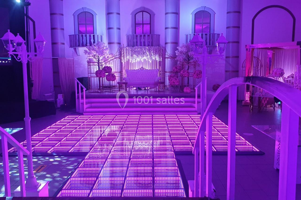 Salle de réception décorée avec des lumières roses, une piste lumineuse et un espace aménagé pour des événements festifs.