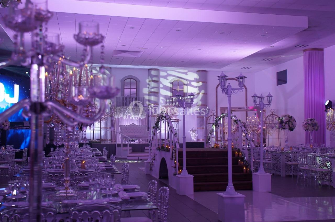 Salle de réception décorée avec des chandeliers, des tables élégantes et un éclairage violet tamisé.
