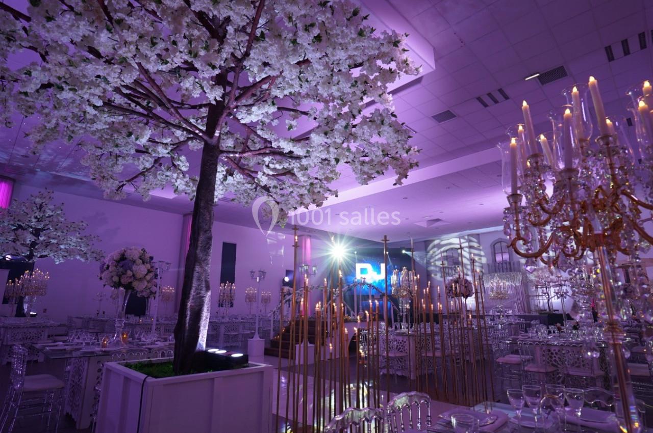Salle de réception élégante avec décorations lumineuses, chandeliers dorés et arbres artificiels fleuris.