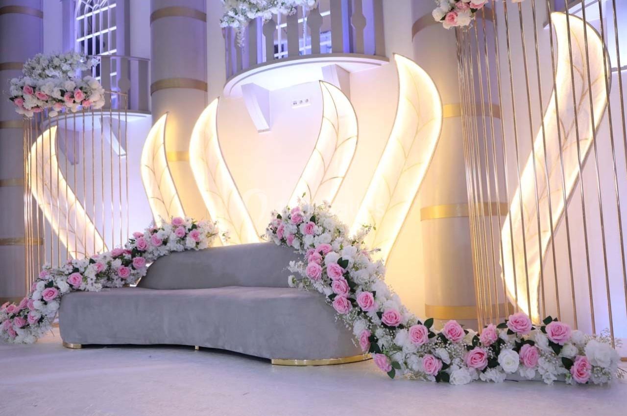 Décor lumineux avec un canapé gris entouré de fleurs roses et blanches, devant des structures dorées et éclairées.