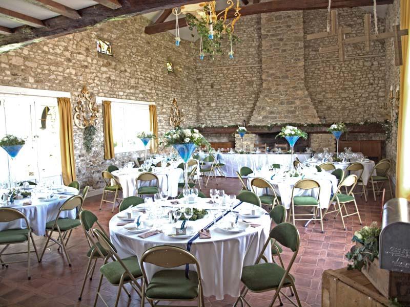 Salle de réception en pierre avec tables rondes dressées, chaises pliantes et décoration florale élégante.