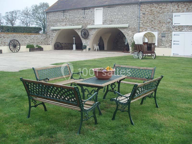 Mobilier de jardin en métal et bois disposé sur une pelouse devant un bâtiment en pierre avec une charrette en arrière-plan.