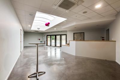 Terrasse avec tables, chaises et parasols, bordée d'une pelouse et d'un bâtiment moderne, sous un ciel ensoleillé.