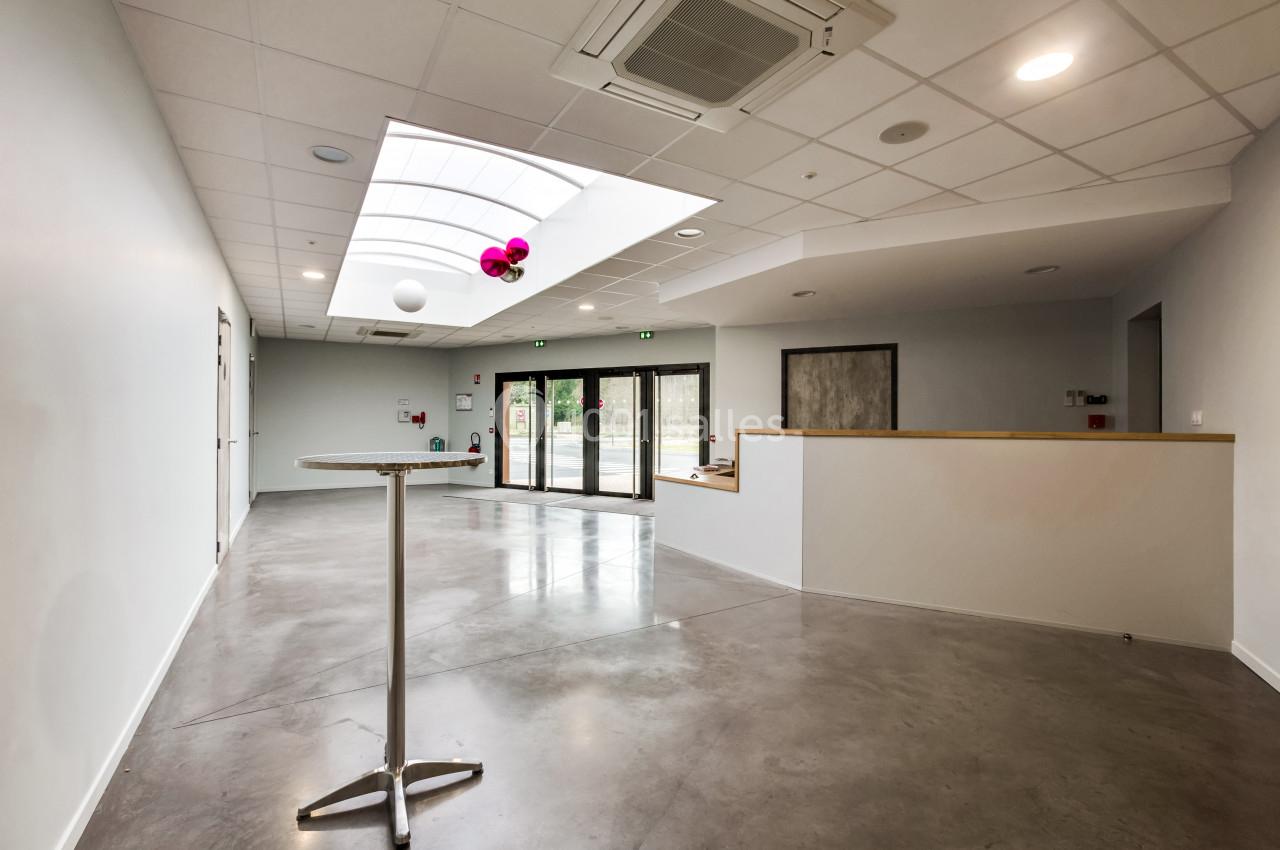 Intérieur d'une salle lumineuse avec sol en béton, table haute, plafond à puits de lumière et porte vitrée donnant sur l…