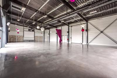 Terrasse avec tables, chaises et parasols, bordée d'une pelouse et d'un bâtiment moderne, sous un ciel ensoleillé.