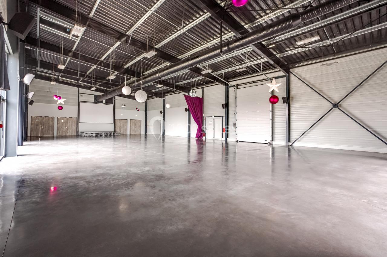 Salle spacieuse avec sol en béton, plafond métallique, rideau violet et décorations suspendues.