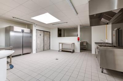 Terrasse avec tables, chaises et parasols, bordée d'une pelouse et d'un bâtiment moderne, sous un ciel ensoleillé.