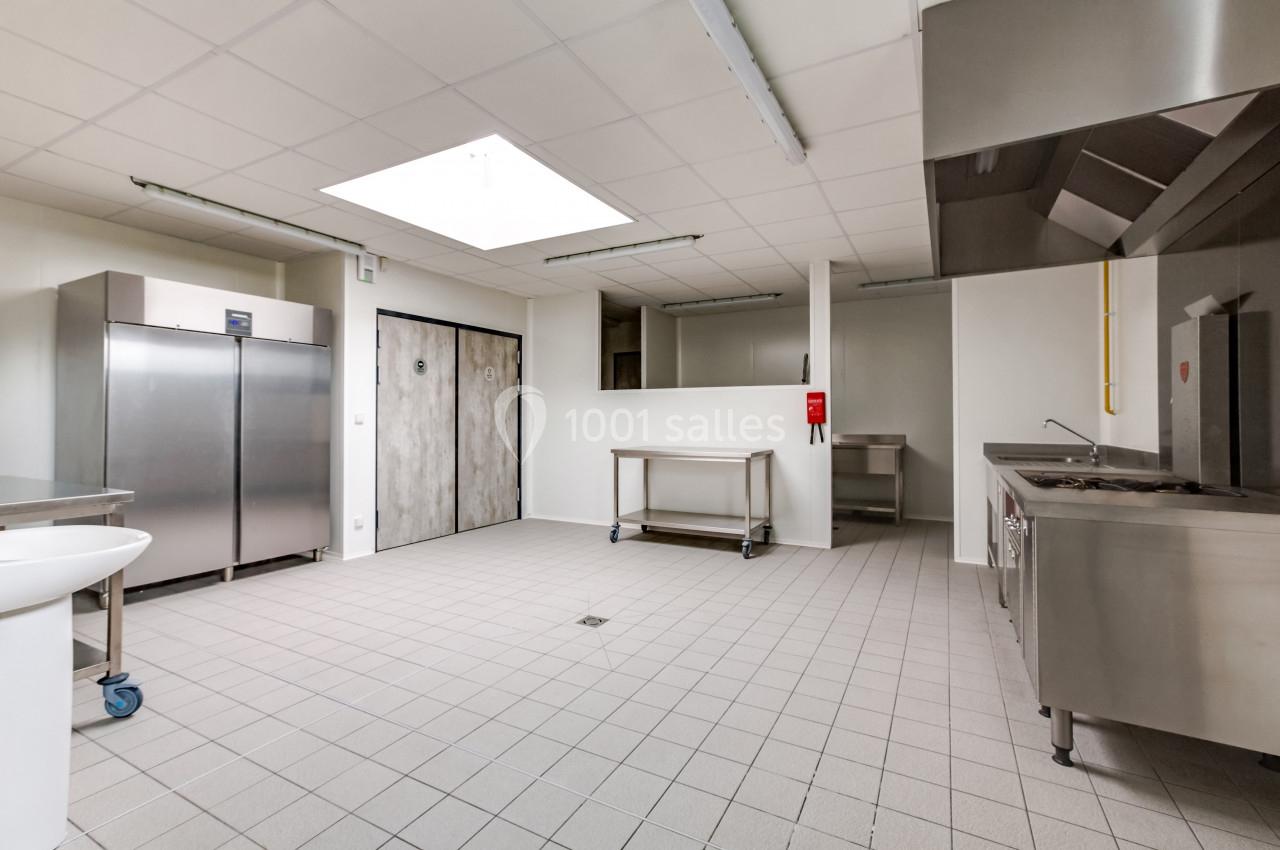 Cuisine professionnelle avec équipements en inox, sol carrelé, éclairage naturel par une grande verrière au plafond.