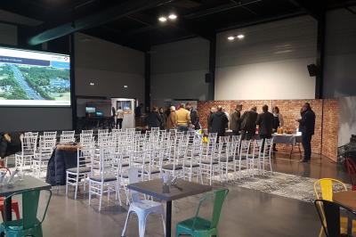Terrasse avec tables, chaises et parasols, bordée d'une pelouse et d'un bâtiment moderne, sous un ciel ensoleillé.