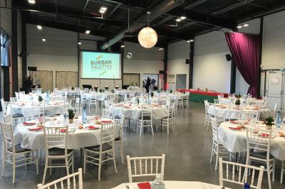 Terrasse avec tables, chaises et parasols, bordée d'une pelouse et d'un bâtiment moderne, sous un ciel ensoleillé.