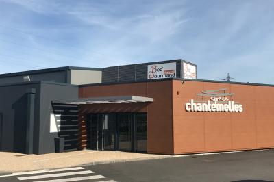 Terrasse avec tables, chaises et parasols, bordée d'une pelouse et d'un bâtiment moderne, sous un ciel ensoleillé.