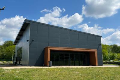Terrasse avec tables, chaises et parasols, bordée d'une pelouse et d'un bâtiment moderne, sous un ciel ensoleillé.