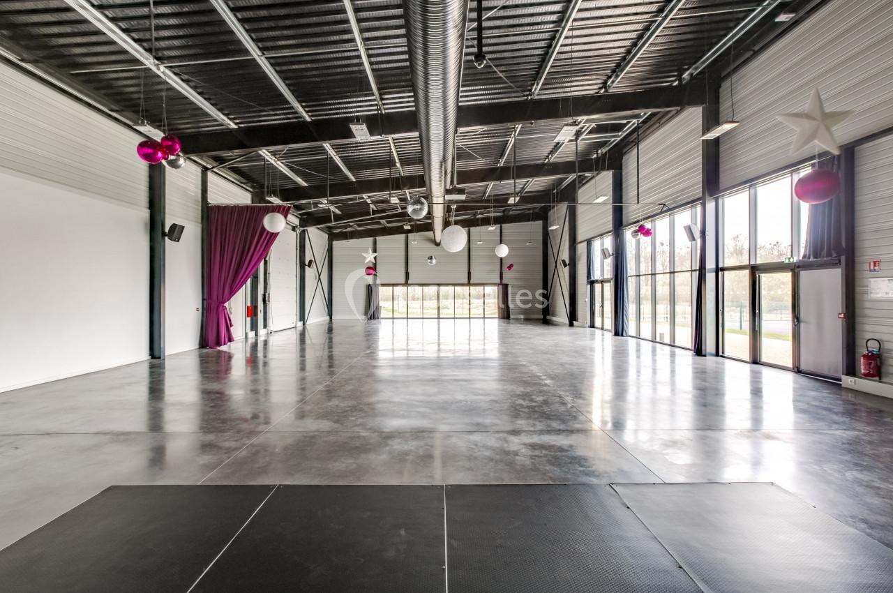 Intérieur d'une grande salle moderne avec sol en béton, murs blancs, rideaux violets et décorations suspendues.
