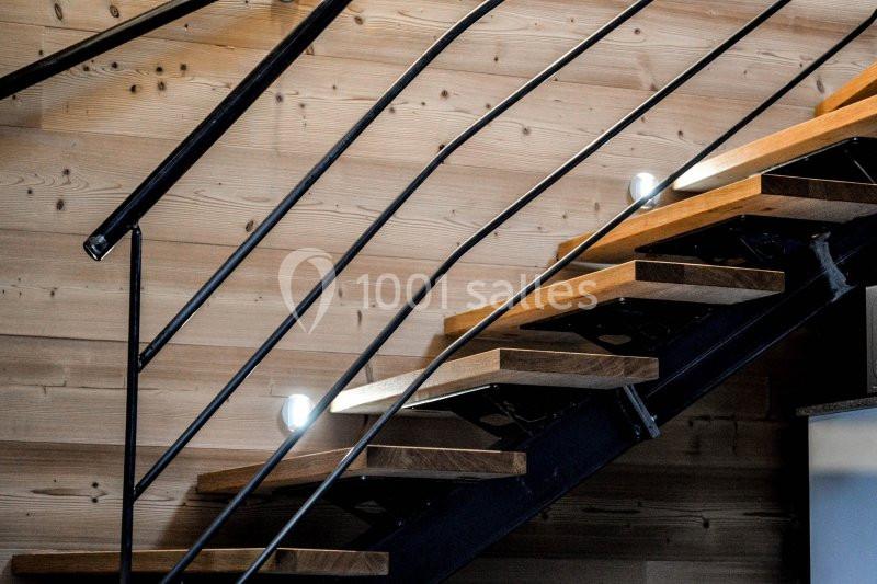 Escalier en bois avec structure métallique noire, éclairé par des spots, contre un mur en bois clair.