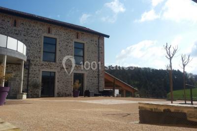 Façade en pierre d'une maison rénovée avec terrasse, grandes fenêtres et espace extérieur gravillonné.