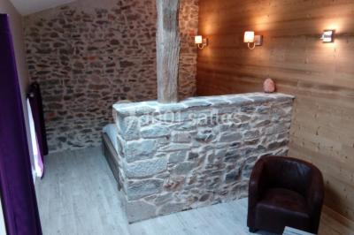 Façade en pierre d'une maison rénovée avec terrasse, grandes fenêtres et espace extérieur gravillonné.