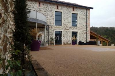 Façade en pierre d'une maison rénovée avec terrasse, grandes fenêtres et espace extérieur gravillonné.