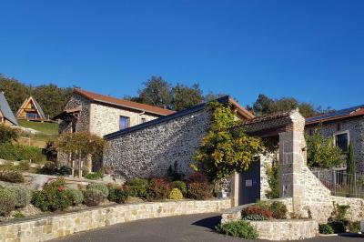Façade en pierre d'une maison rénovée avec terrasse, grandes fenêtres et espace extérieur gravillonné.