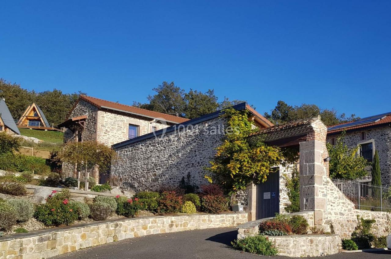 Maison en pierre avec toit en tuiles, entourée de végétation et située dans un environnement rural sous un ciel bleu.