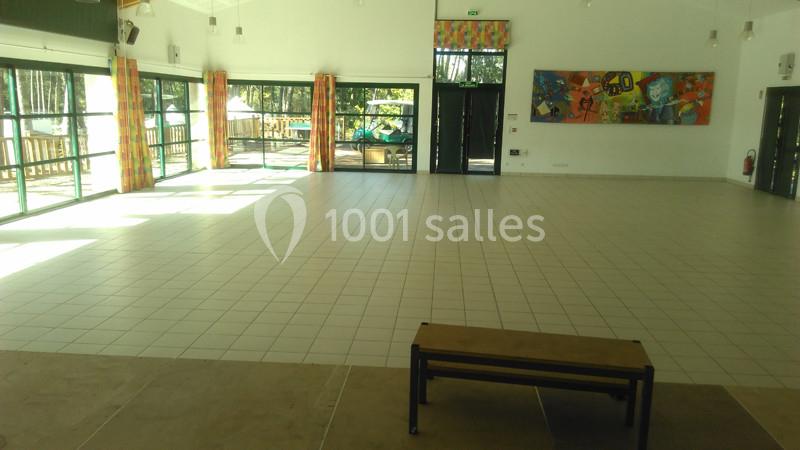 Salle lumineuse avec carrelage clair, grandes baies vitrées, rideaux colorés et un banc au premier plan.