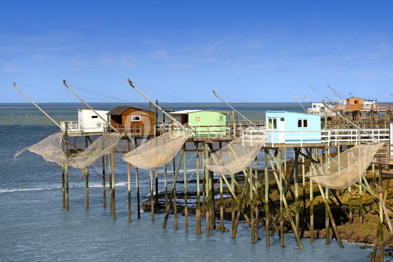 Cabanes de pêche sur pilotis avec filets suspendus, alignées le long d'une côte sous un ciel bleu.