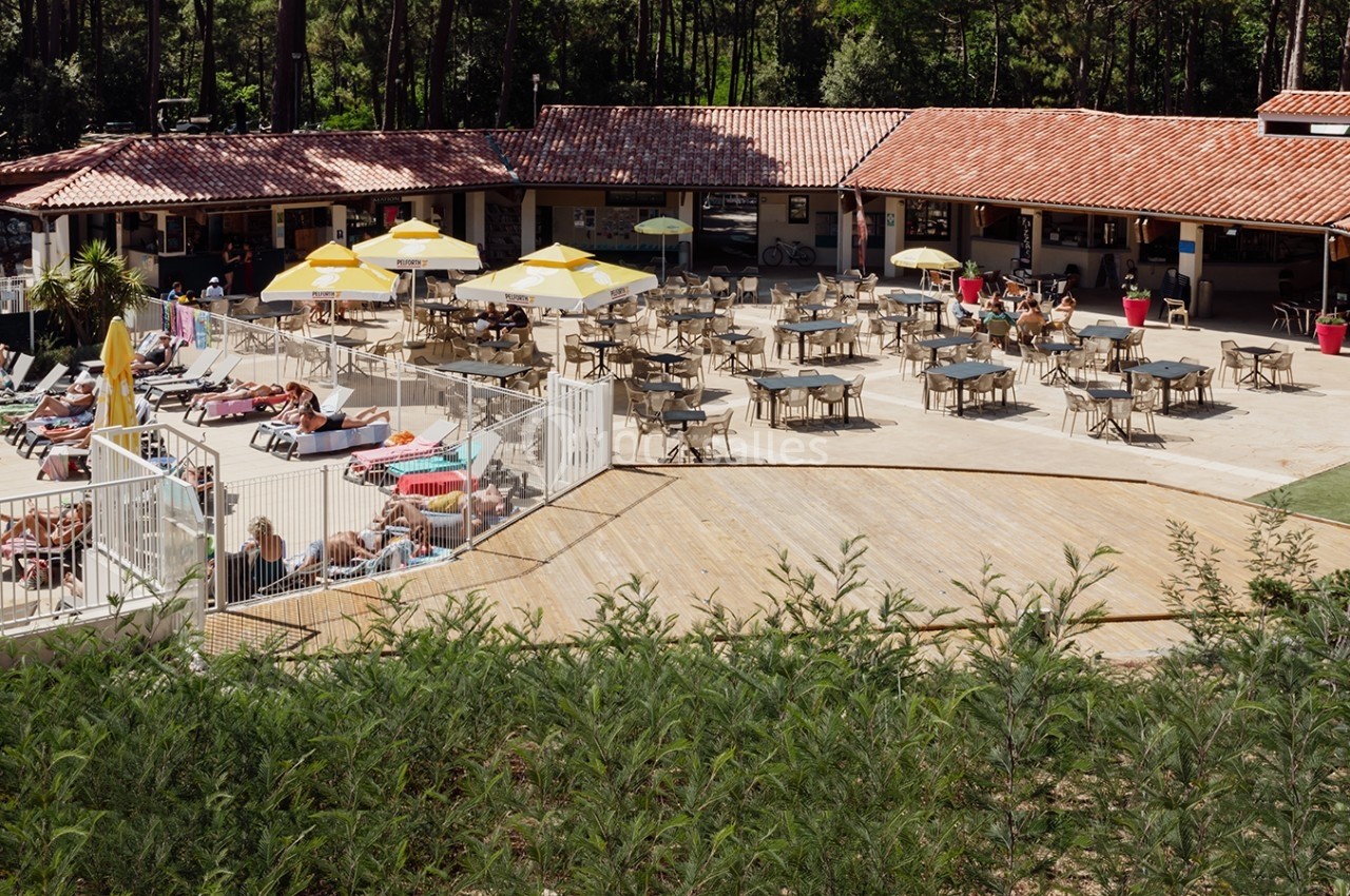 Terrasse d'un restaurant avec tables, chaises et parasols jaunes, près d'une piscine entourée de végétation et de transats.