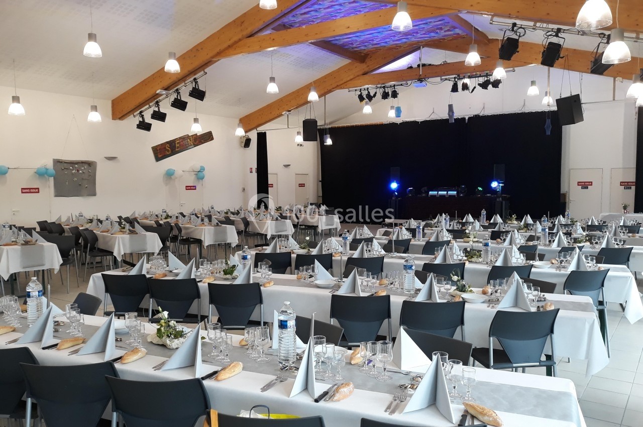 Salle de réception décorée avec des tables dressées pour un événement, éclairage tamisé et scène en arrière-plan.