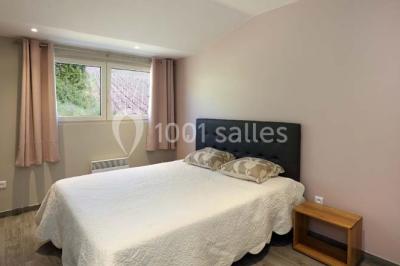 Chambre lumineuse avec deux lits, parquet au sol, murs clairs et fenêtres donnant sur un jardin verdoyant.