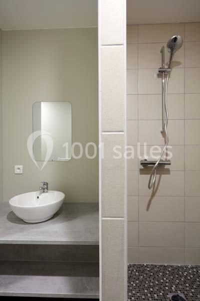 Salle de bain avec lavabo sur plan en béton, miroir mural et douche à l'italienne avec pommeau mural.