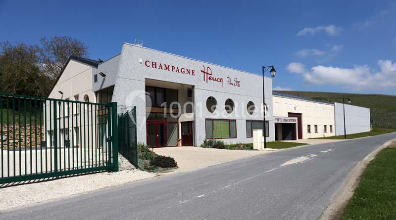 Bâtiment moderne avec enseigne ’Champagne Henry’ et espace de réception, situé en bordure de route sous un ciel bleu.