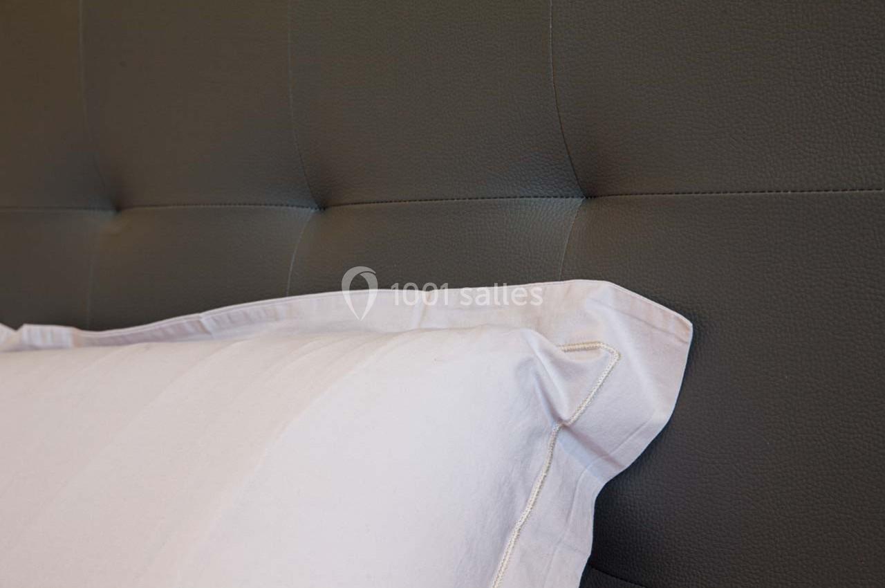 Coussin blanc posé contre une tête de lit capitonnée en cuir gris foncé.