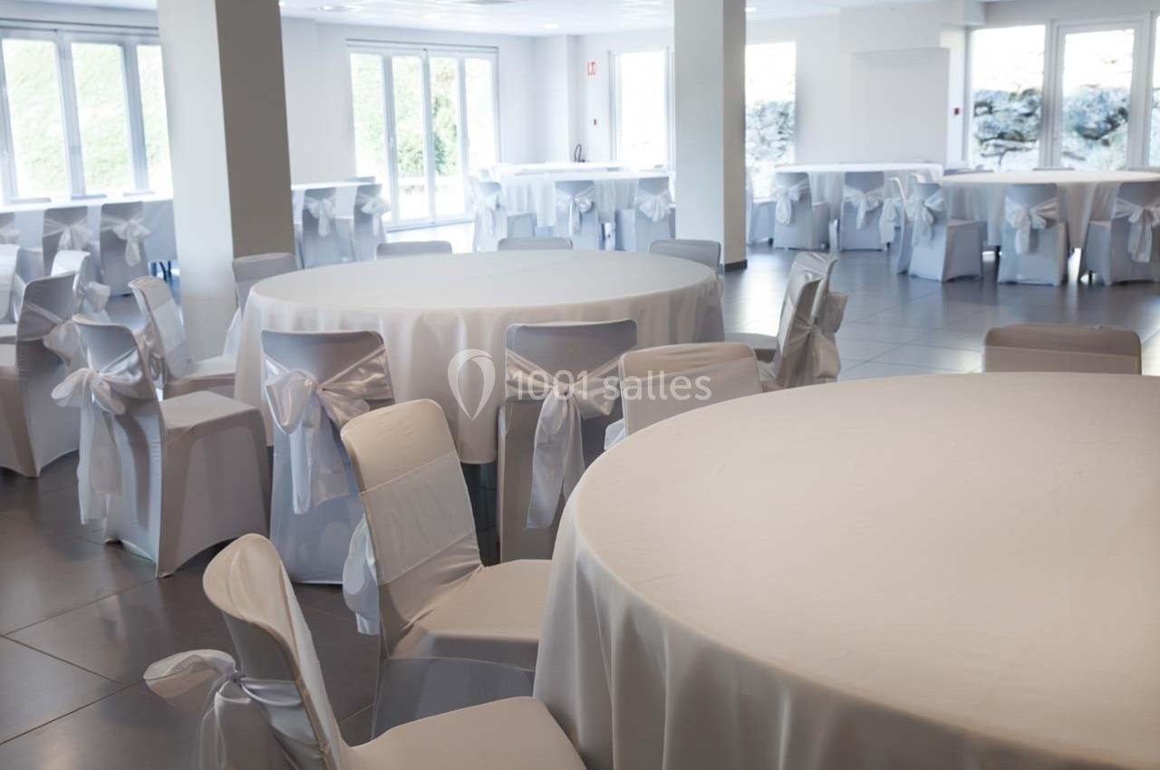 Salle de réception lumineuse avec des tables rondes et des chaises blanches décorées de nœuds.