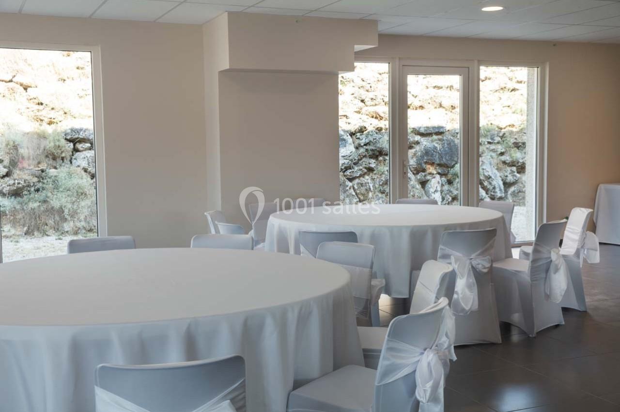 Salle lumineuse avec des tables rondes recouvertes de nappes blanches et des chaises décorées de nœuds.
