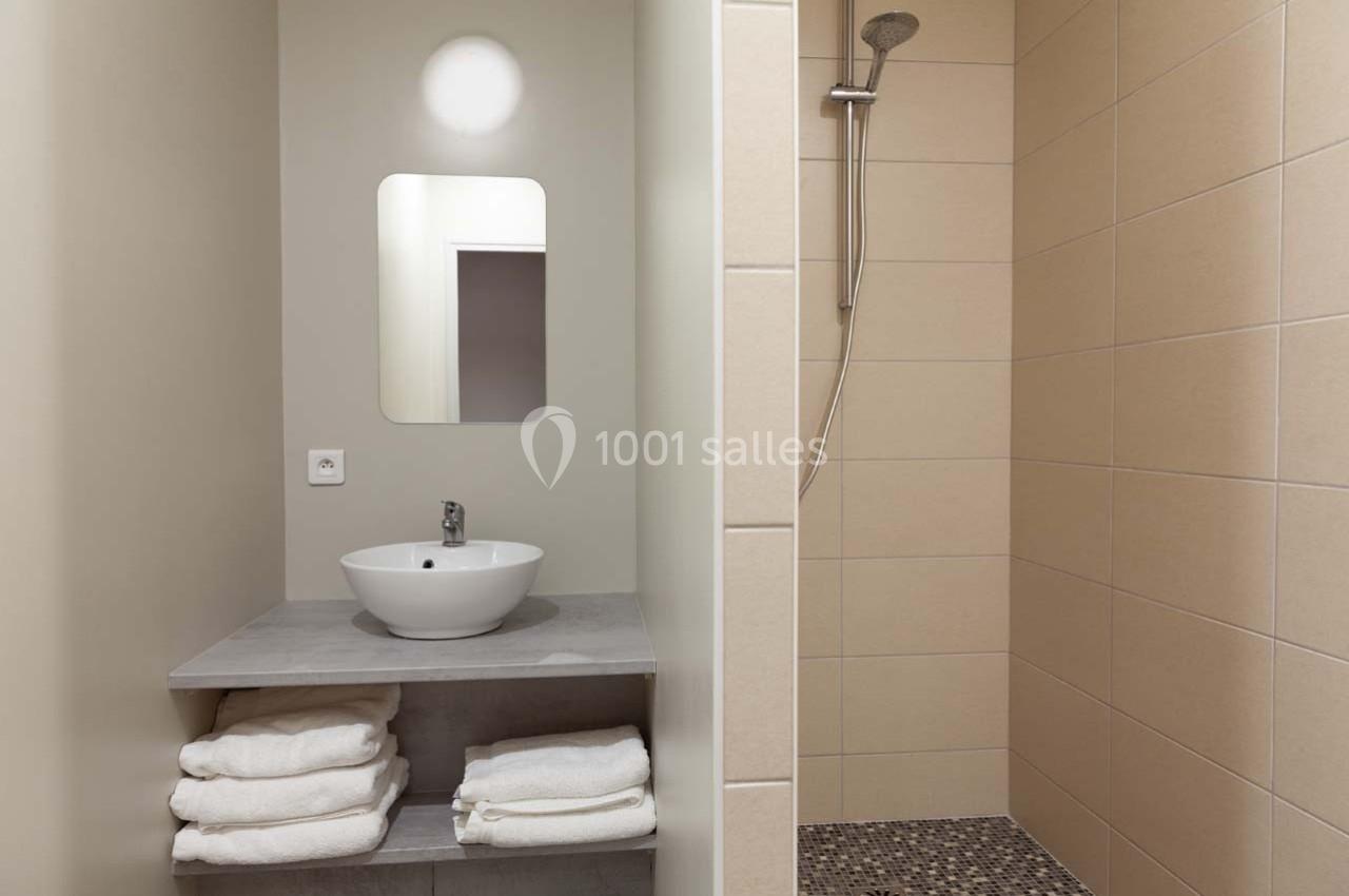 Salle de bain avec lavabo, miroir, étagère contenant des serviettes pliées et douche à l'italienne carrelée.