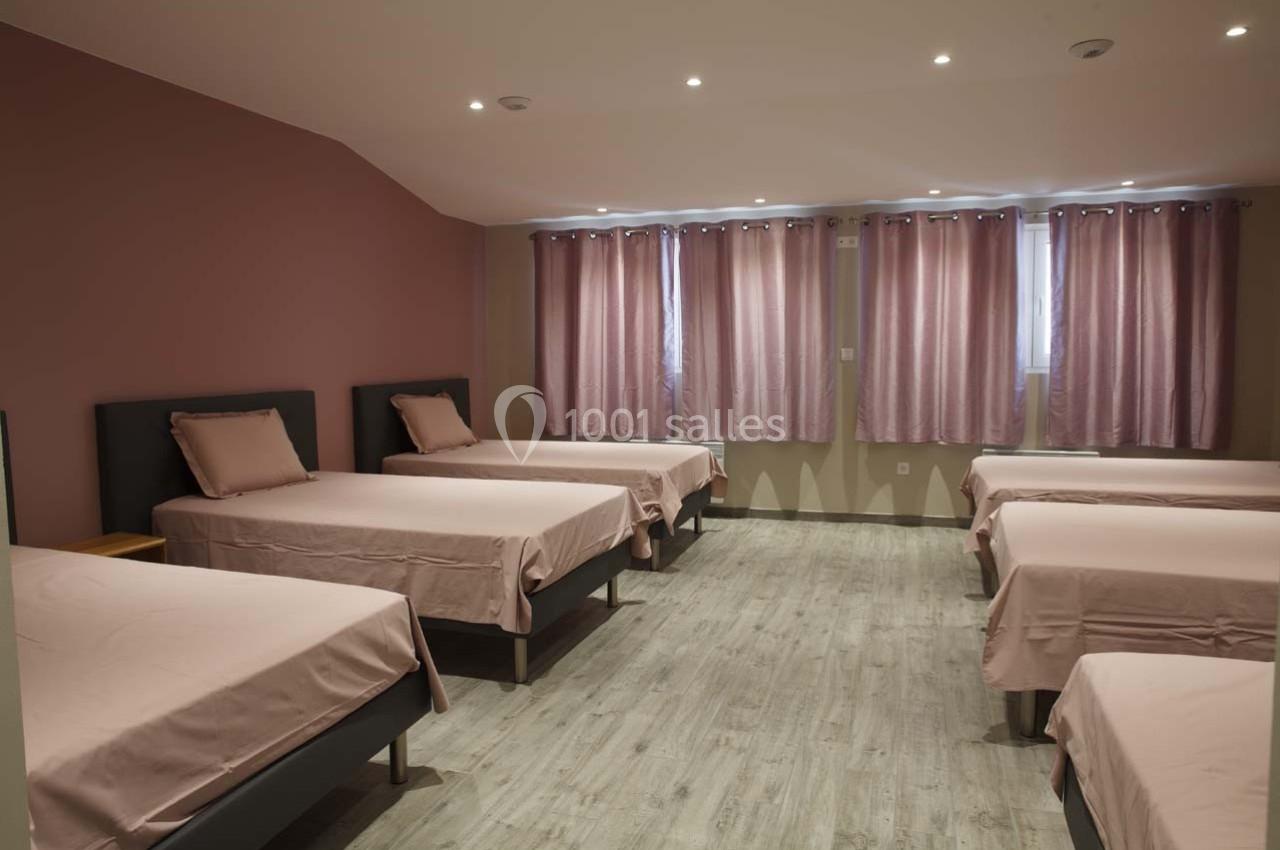 Dortoir avec six lits simples alignés, draps roses assortis aux rideaux, sol en parquet clair.