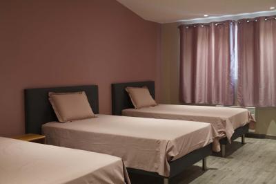 Chambre lumineuse avec deux lits, parquet au sol, murs clairs et fenêtres donnant sur un jardin verdoyant.