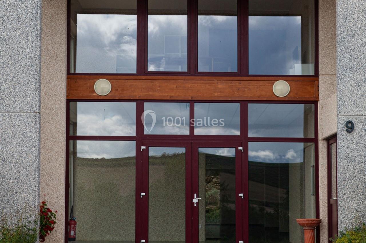 Façade avec une grande porte vitrée encadrée de bois, reflétant le ciel et un paysage extérieur.