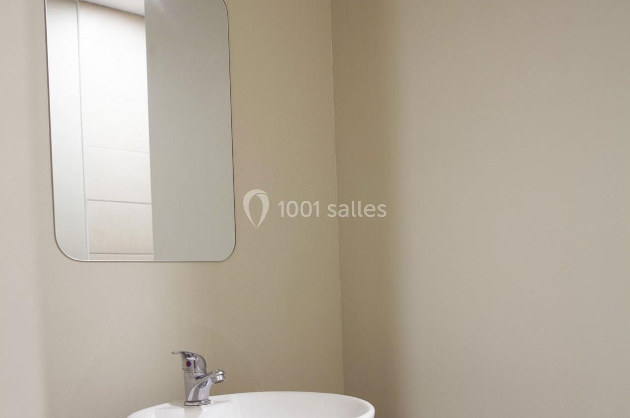 Lavabo blanc avec robinet chromé, surmonté d'un miroir rectangulaire dans une salle de bain aux murs beiges.